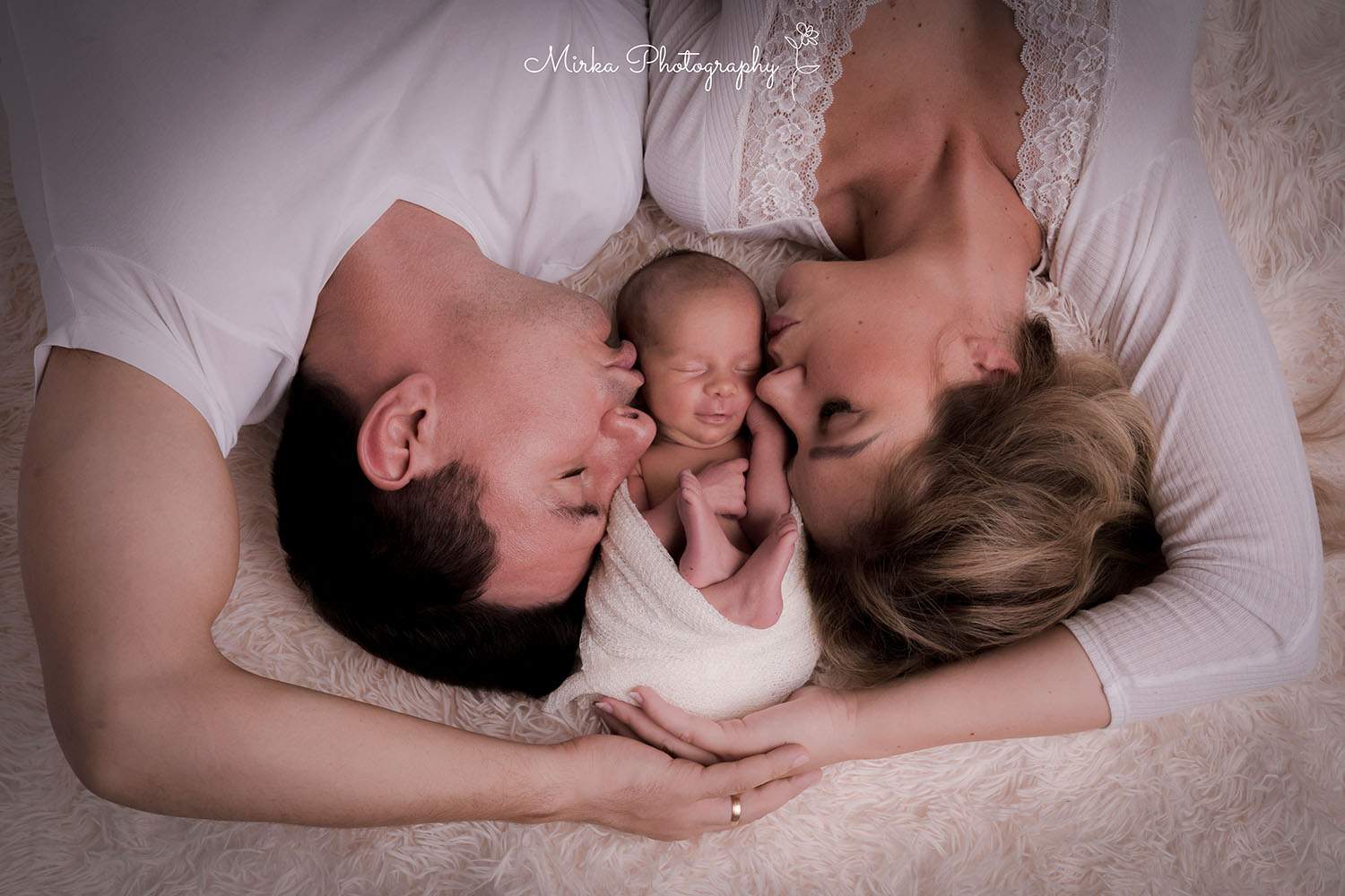 Eltern liegen mit kleinem Baby zwischen sich und mirkaphotography hält das tolle Bild in Kamera fest