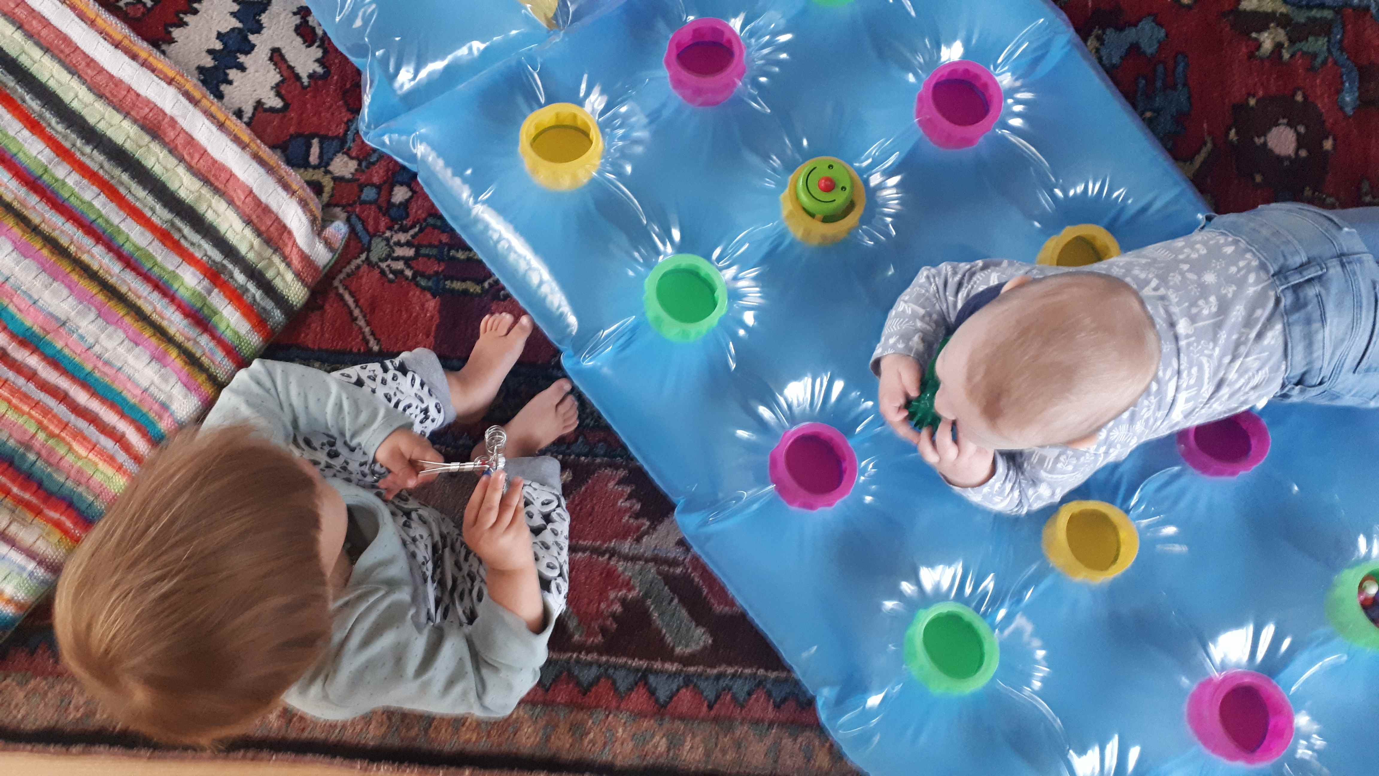 Bild aus der Krabbelgruppe mit 2 Kleinkindern auf einer Luftmatratze mit Spielzeug