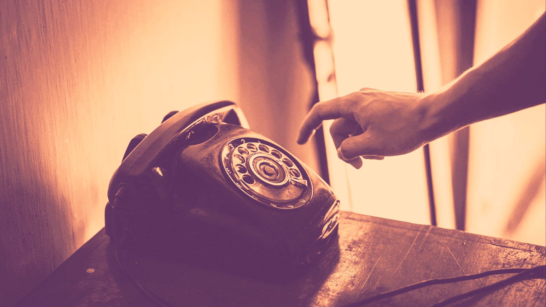 Ein auf einem Möbel stehendes altes Telefon. Eine Hand, welche zum Telefon greift ist sichtbar.