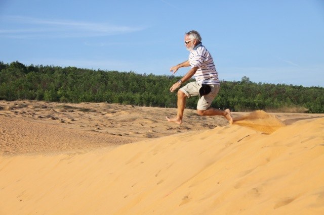 und springt jugendlich dynamisch in den roten Sand!