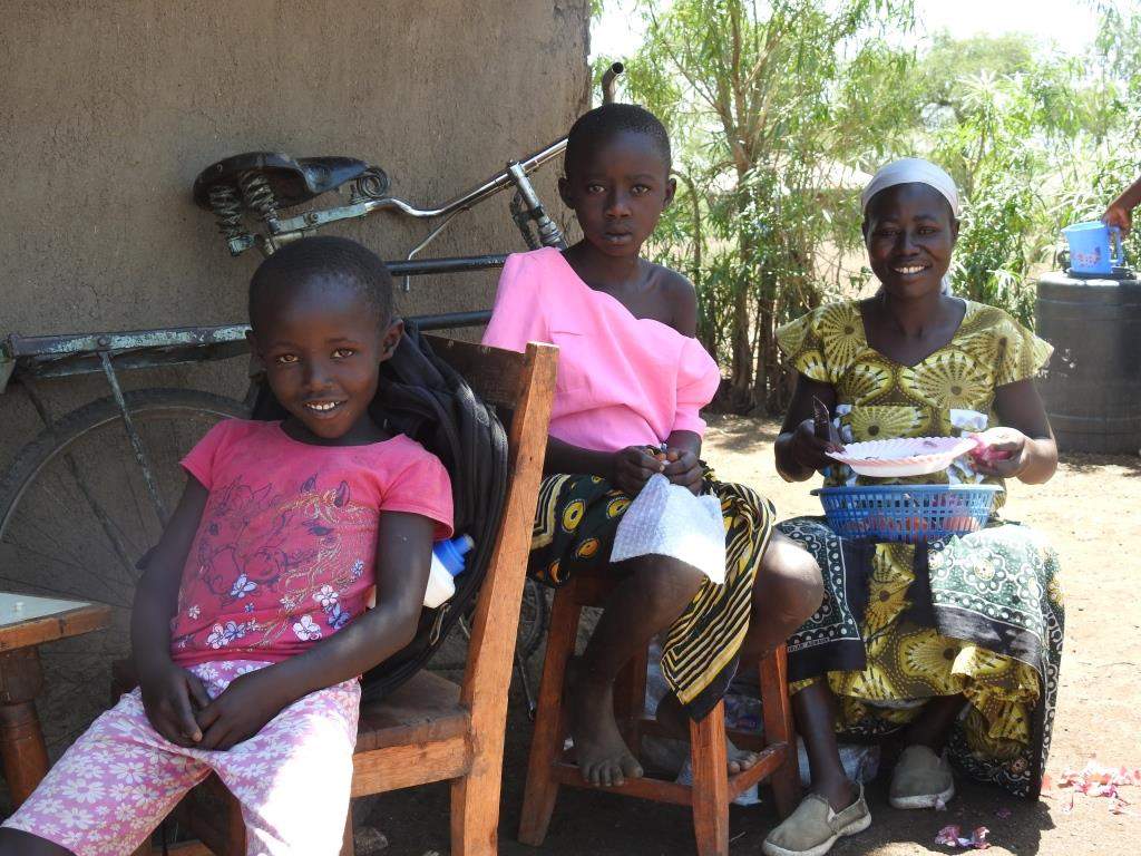 Zwei afrikanische Kinder und ihre Mutter aus Kenia sitzen vor ihrem Haus und lachen für die Kamera
