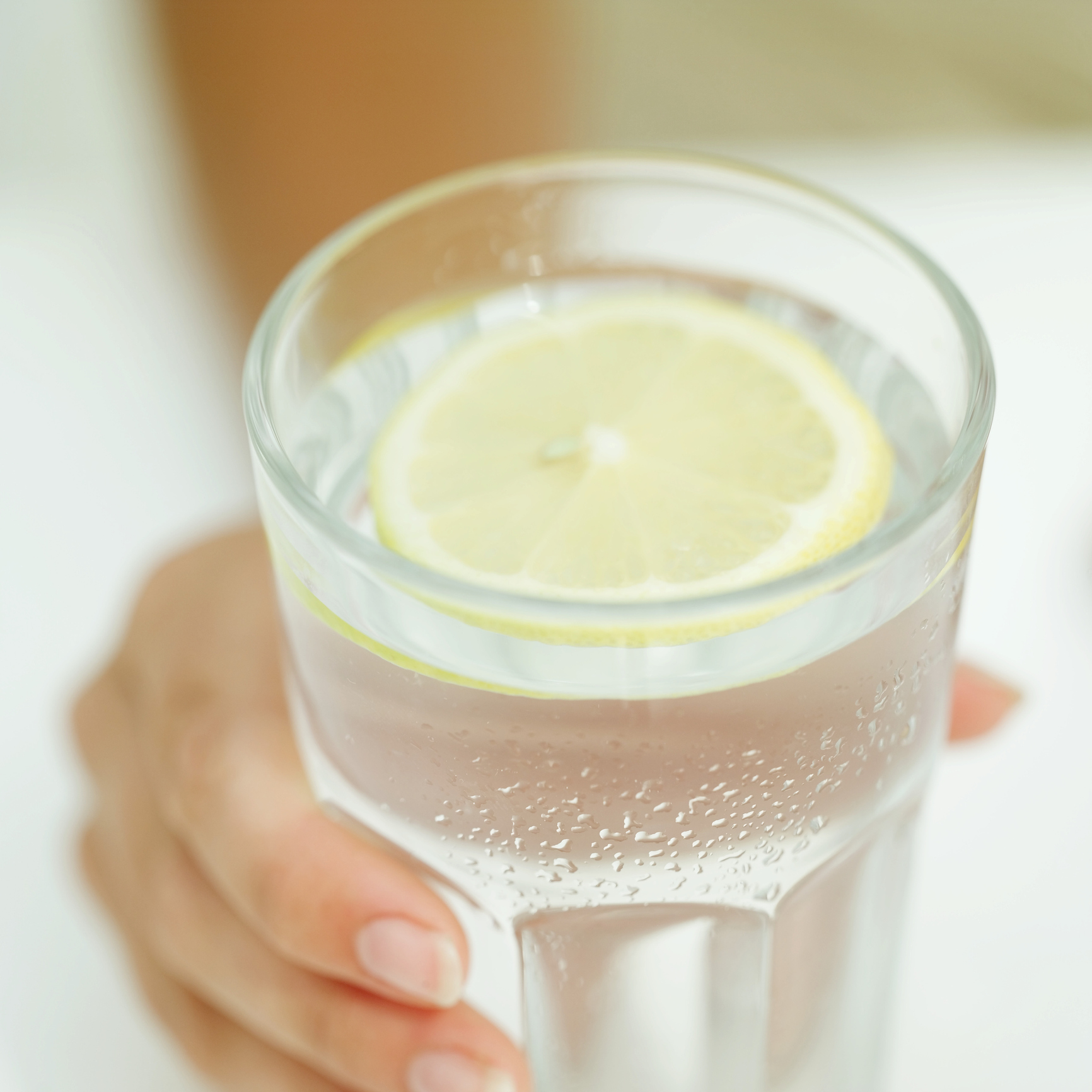 close-up-of-a-woman-s-hand-holding-a-glass-of-water-with-a-lemon-wedgejpg