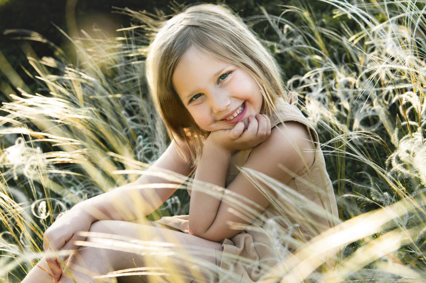 Fotografie, Kinder und Familie in Wien Umgebung:hier ein lachendes Mädchen das in der Wiese sitzt bei Sonnenschein.