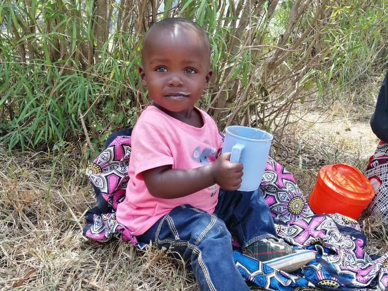 Ein kleines afrikanisches Kind aus Kenia trinkt aus einem blauen Becher und lächelt