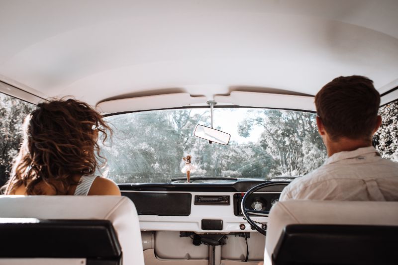 Zwei Personen sitzen in einem Auto, Bäume sind durch die Windschutzscheibe zu sehen